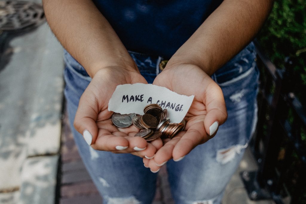 Photo of a person's hands being held out, full of coins and a piece of paper with "make change" written on it in black marker.